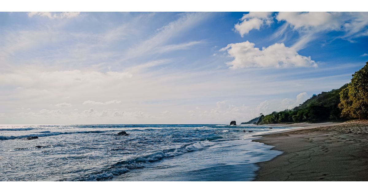 A serene beach scene in Santa Teresa, Costa Rica, with gentle waves, a cloudy sky, and lush greenery along the shoreline.