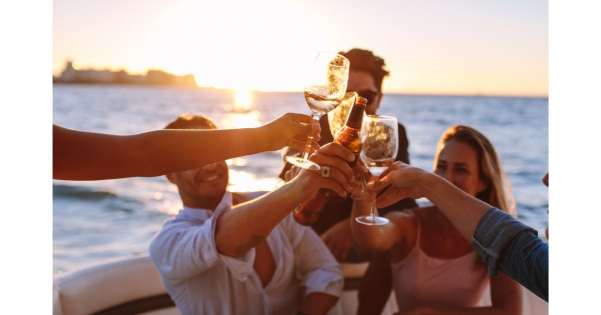 A group of people toasting with drinks on a yacht at sunset, celebrating together in a luxury setting.