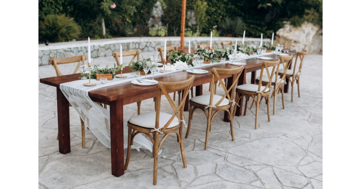 A beautifully set outdoor dining table with wooden chairs, candles, and floral arrangements, perfect for a gathering or special event.