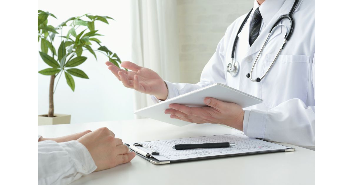 A doctor holding a medical folder while speaking with a patient, with a stethoscope around their neck and a plant in the background, symbolizing healthcare consultation and communication.