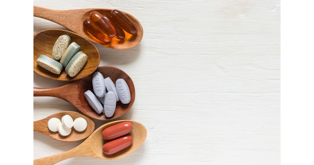 A variety of oral supplements, including capsules, tablets, and soft gels, arranged on wooden spoons against a white background.