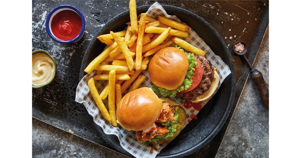 Two delicious burgers with fresh lettuce and tomato, served with crispy golden fries and dipping sauces on the side.