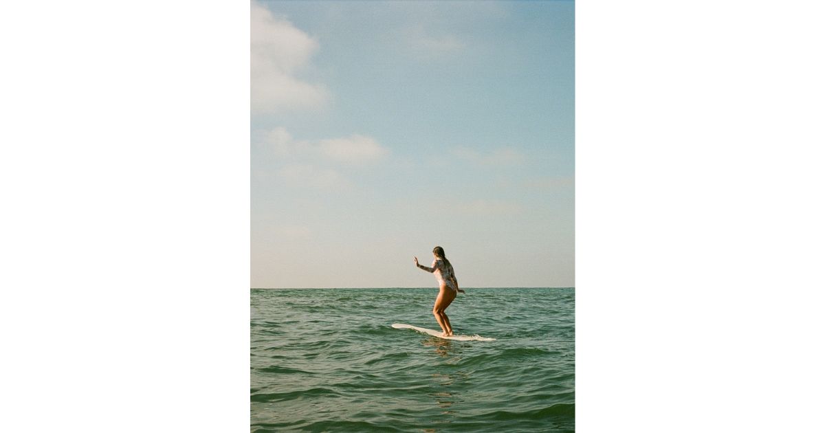 A woman surfing on a longboard in the ocean, balancing gracefully on the waves under a clear blue sky.