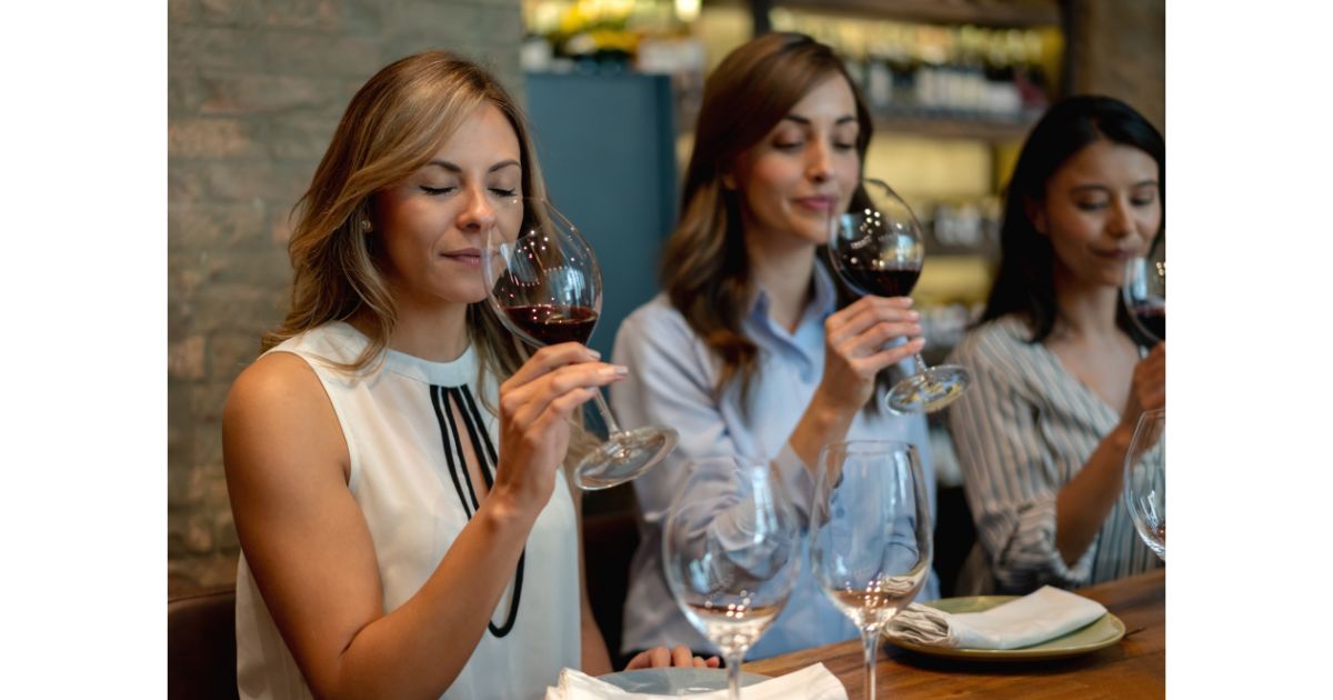 Three women enjoying a wine tasting, savoring the aroma of their glasses in a cozy, well-lit setting.