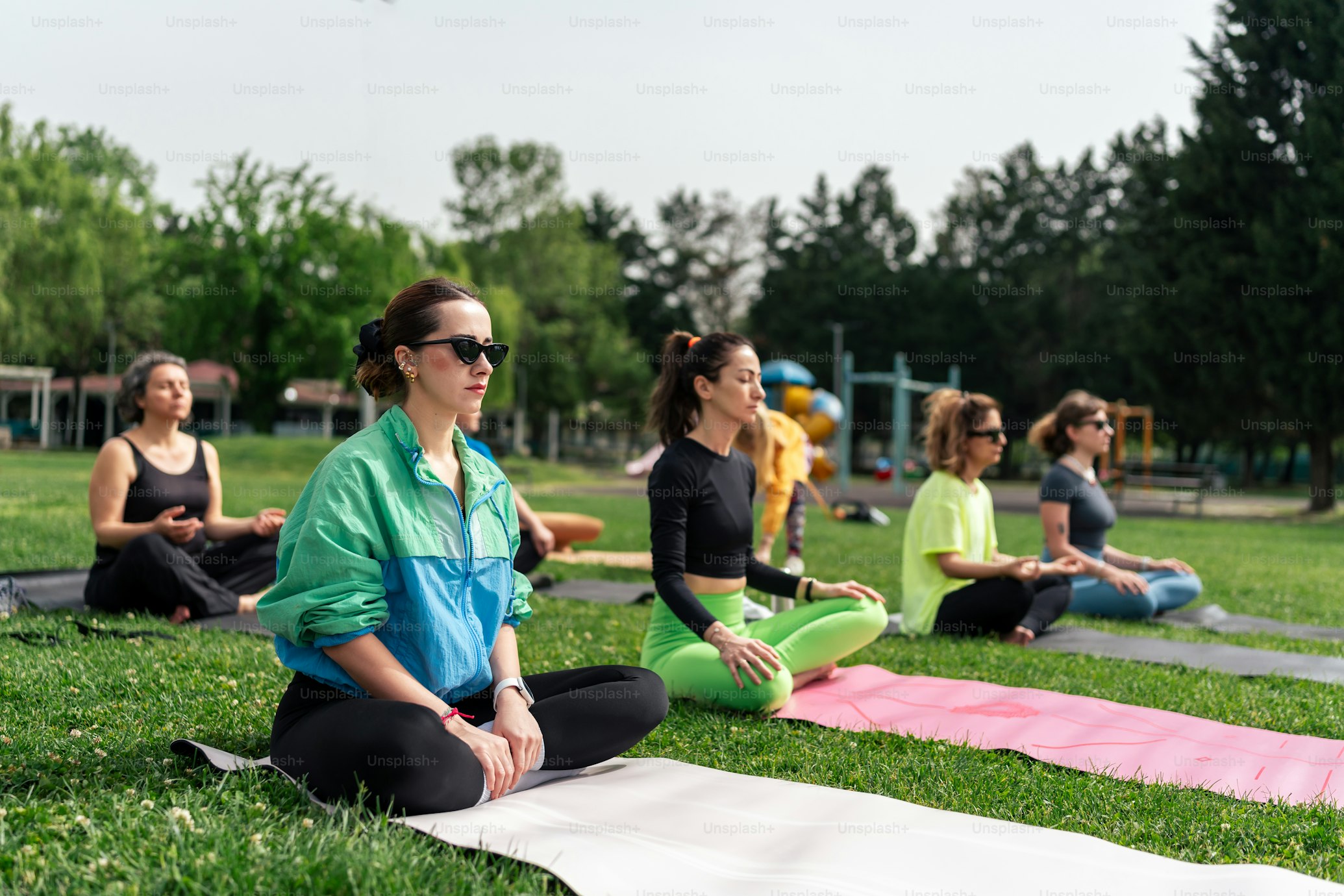 A group of people practicing yoga outdoors in a park, sitting cross-legged on yoga mats, with a focus on relaxation and mindfulness.