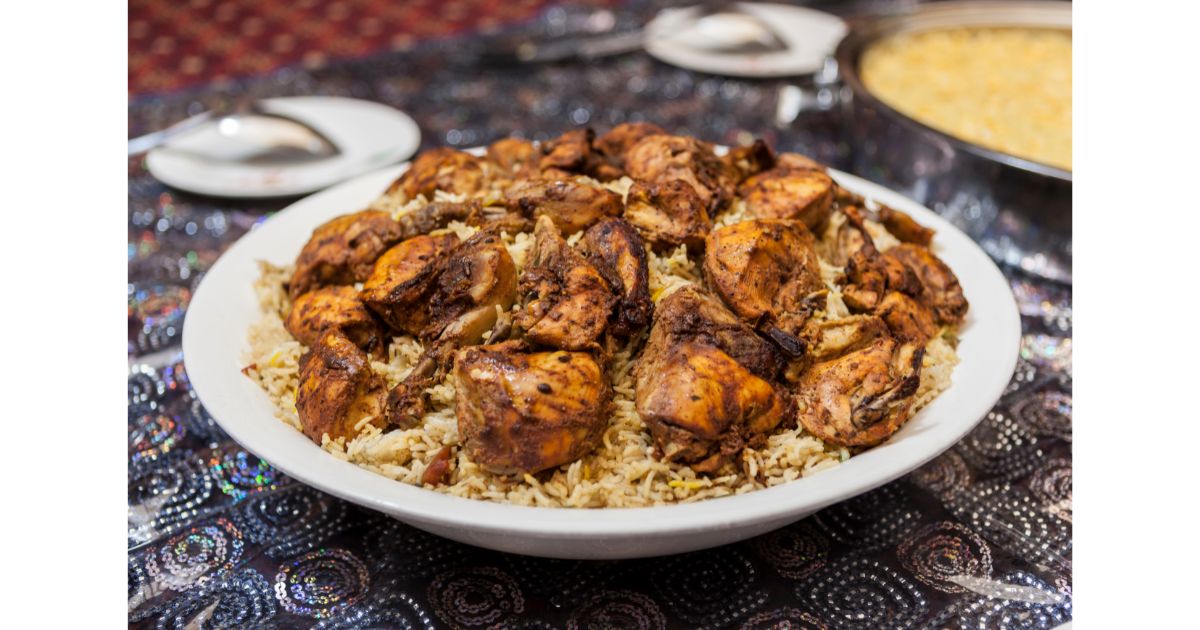 A plate of flavorful grilled chicken served over a bed of rice, presented on a decorative tablecloth with a side dish in the background.