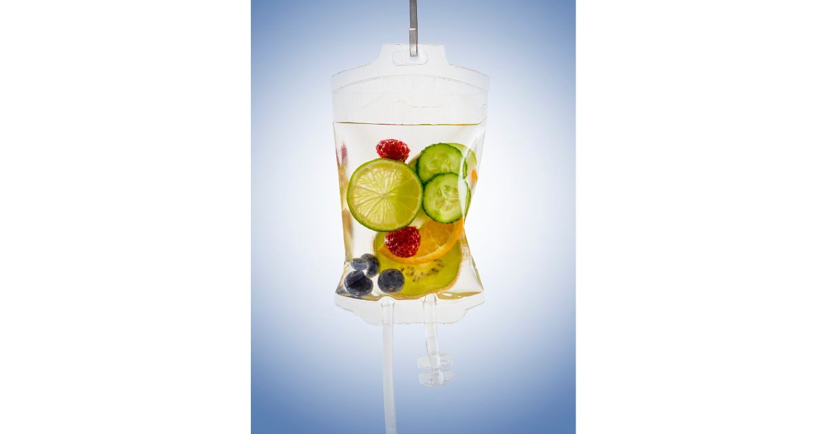 An IV bag filled with infused water and slices of fruits like lime, cucumber, orange, and berries, symbolizing hydration and wellness.