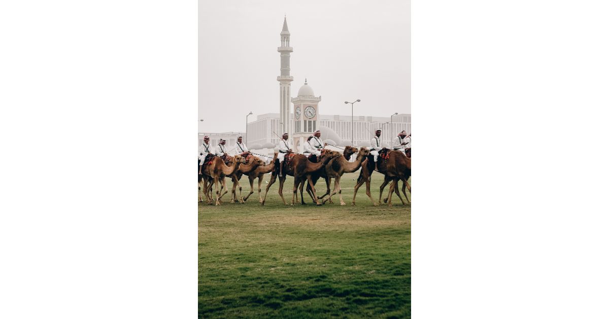 A group of people riding camels in front of a large clock tower in Doha, Qatar.