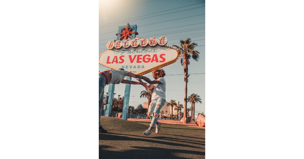 Two people joyfully holding hands in front of the iconic 'Welcome to Fabulous Las Vegas' sign, capturing a fun moment with palm trees and bright skies.