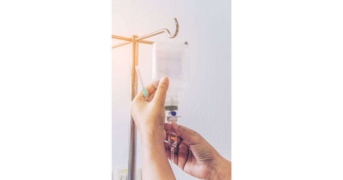 Close-up of hands adjusting an IV drip bag on a metal stand, preparing for intravenous therapy.