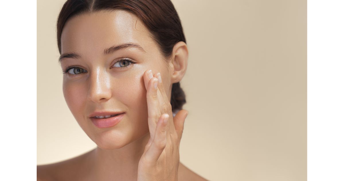 A close-up of a woman gently applying skincare to her face, showcasing a smooth and radiant complexion. She appears relaxed and confident in her skin health.