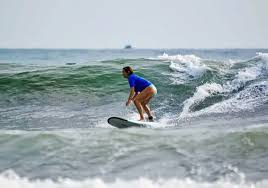 A person surfing on a wave at Playa Hermosa, wearing a blue rash guard and shorts, showcasing the excitement of riding the ocean's waves.