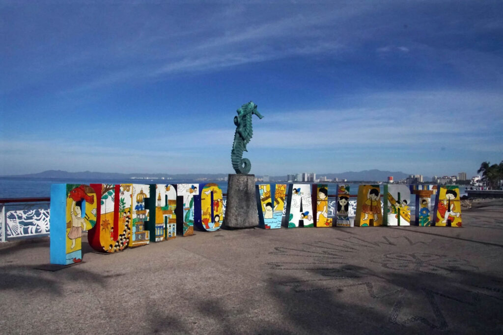 Colorful "Puerto Vallarta" sign with artistic designs, featuring a seahorse statue in the background along the scenic oceanfront promenade.
