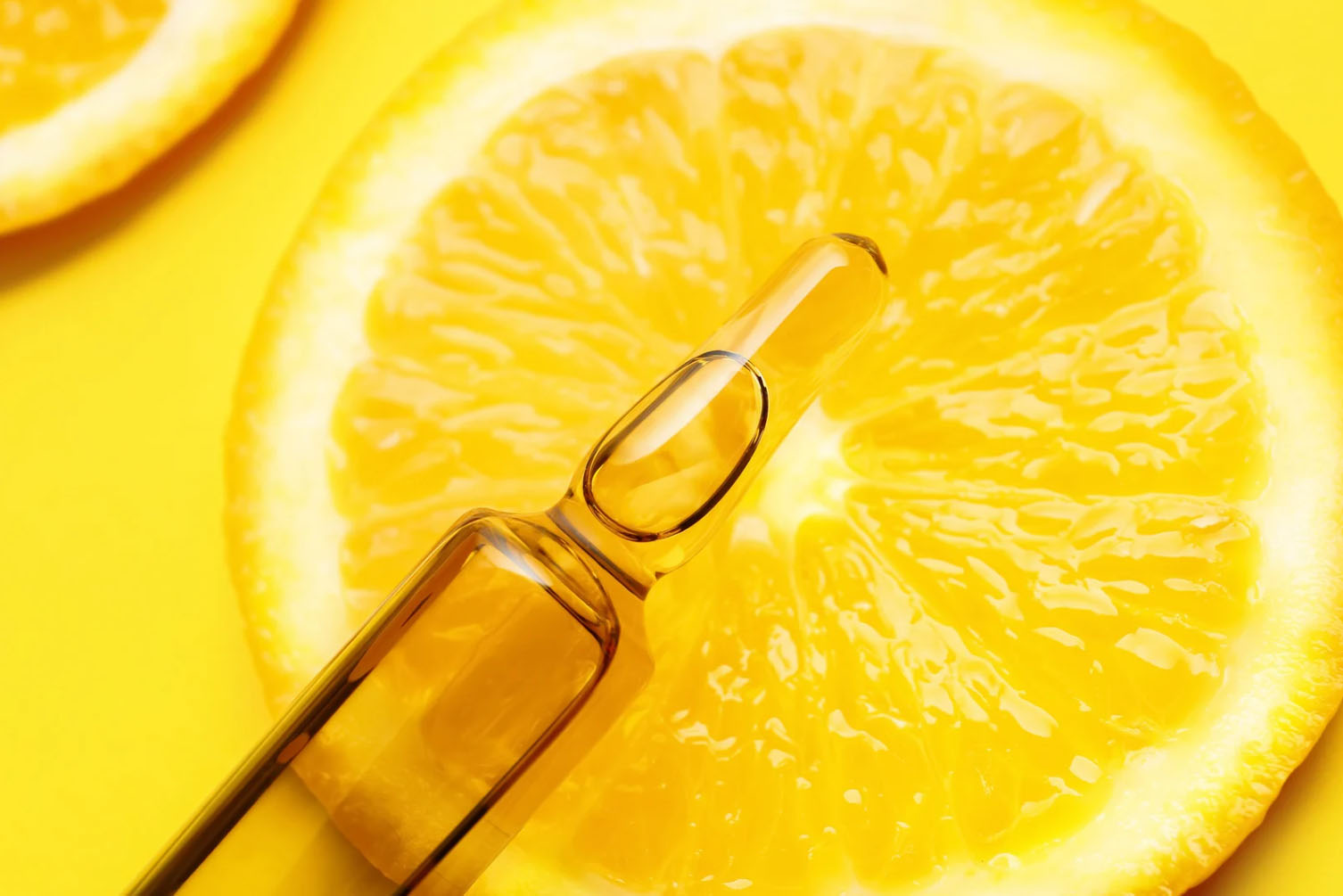 Close-up of a vitamin ampoule placed on top of a fresh orange slice, with a bright yellow background.