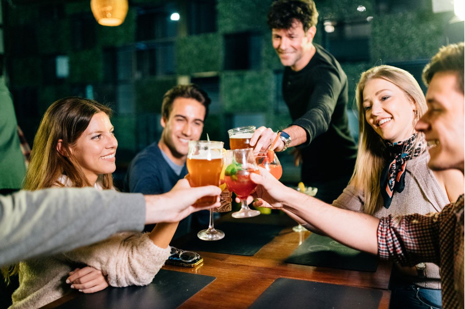 Group of friends toasting with drinks around a table, celebrating and having fun.