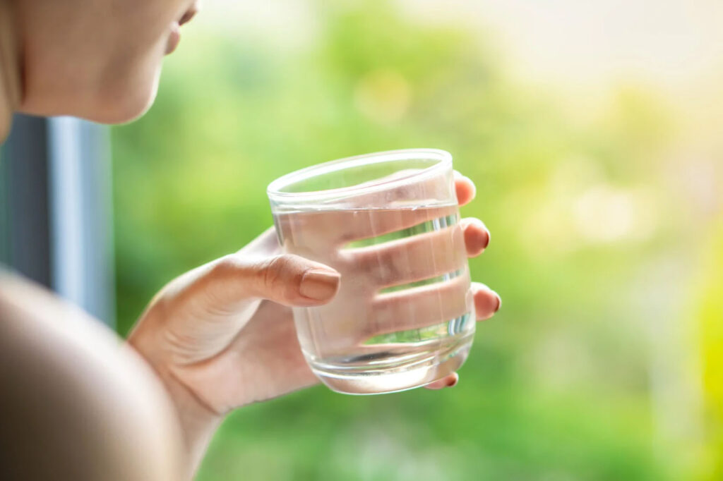 A person holding a glass of water with a blurred green background.