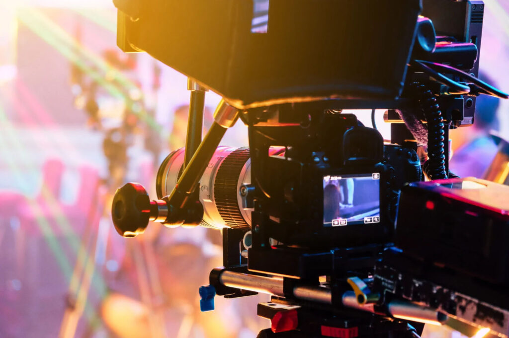 Professional video camera filming a colorful, brightly lit scene at a film festival or studio set.
