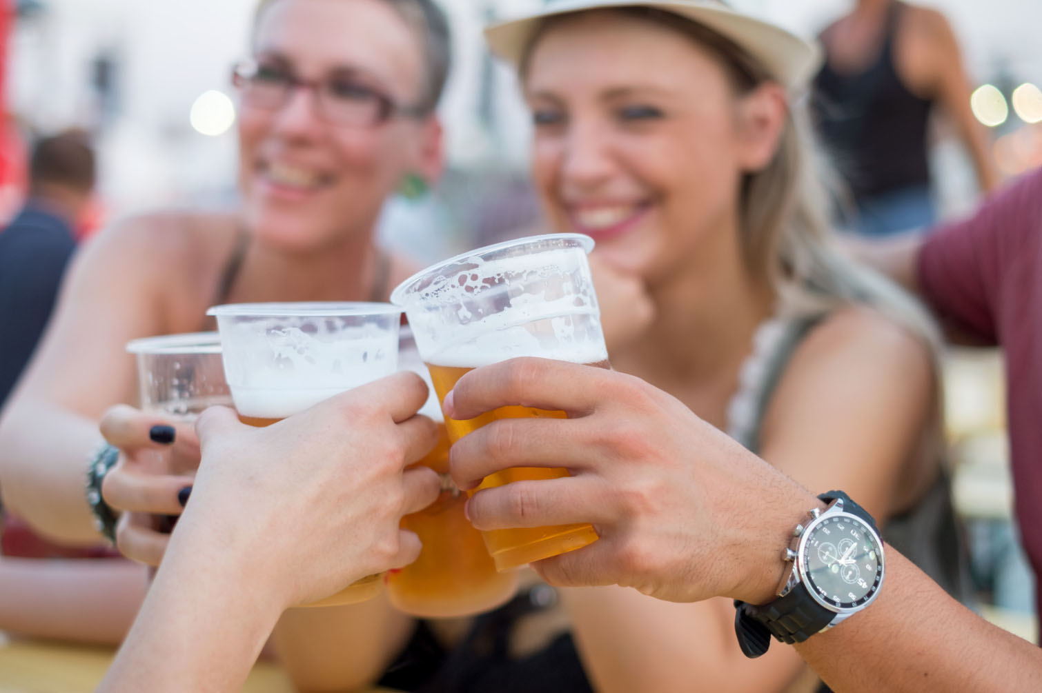 A group of friends cheers with plastic cups filled with beer, enjoying the festive atmosphere at an outdoor event, smiling and celebrating together.