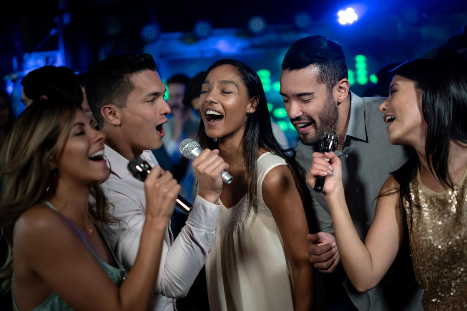 A group of friends singing together at a lively karaoke party with microphones in hand, enjoying the vibrant lights and music in the background.