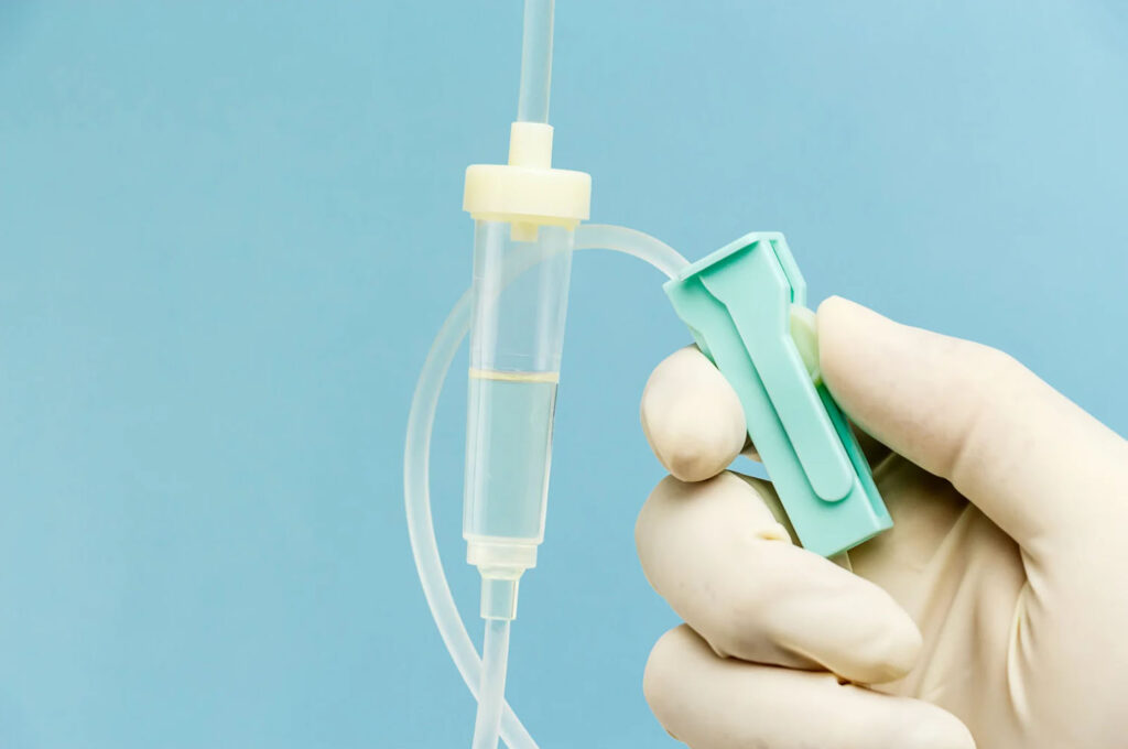 A close-up image of a hand holding an IV drip with a tube, showcasing a medical IV setup against a light blue background.