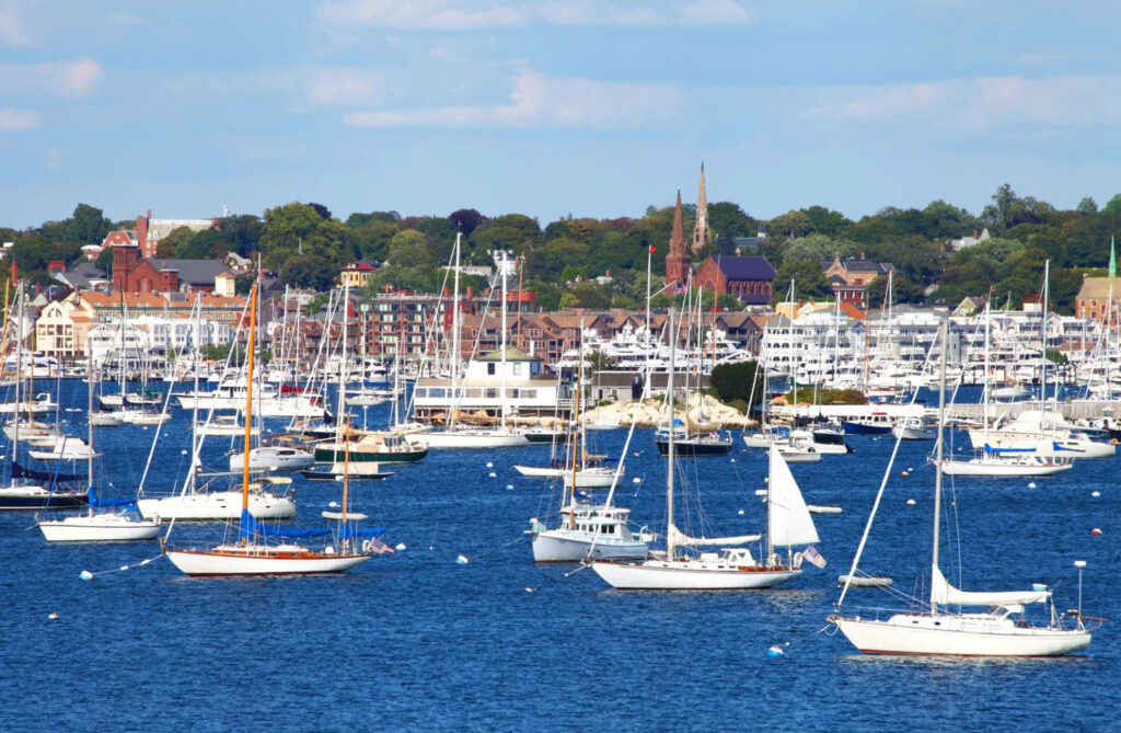 A scenic view of a harbor filled with sailboats, with a picturesque town in the background and clear blue skies above.
