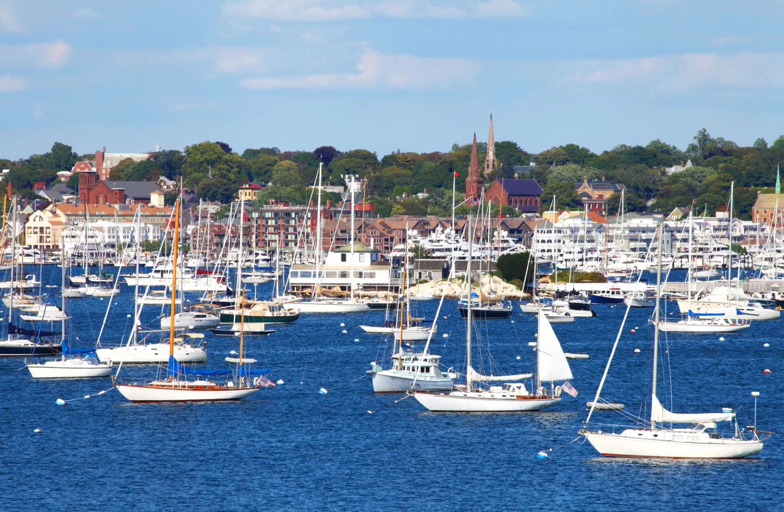 A scenic view of a harbor filled with sailboats, with a picturesque town in the background and clear blue skies above.