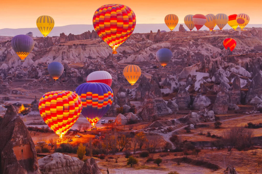 A vibrant scene of multiple hot air balloons soaring over rocky landscapes during sunrise, with colorful patterns against the soft morning light.
