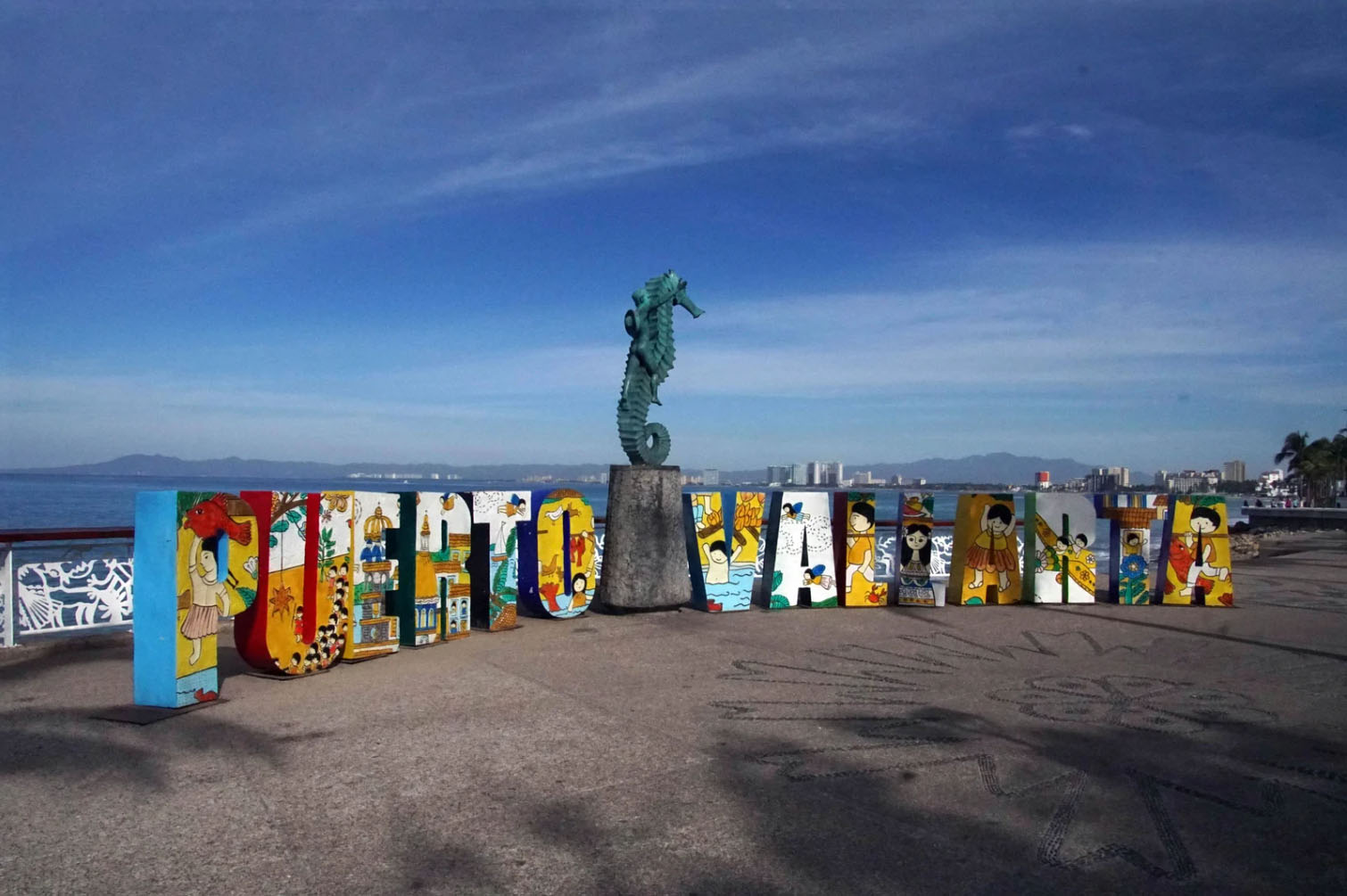 Colorful "Puerto Vallarta" sign on the Malecón, with a scenic view of the ocean and mountains in the background.