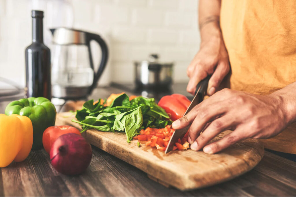 Person chopping fresh vegetables on a cutting board in a kitchen, symbolizing healthy eating, meal preparation, and nutritional wellness.
