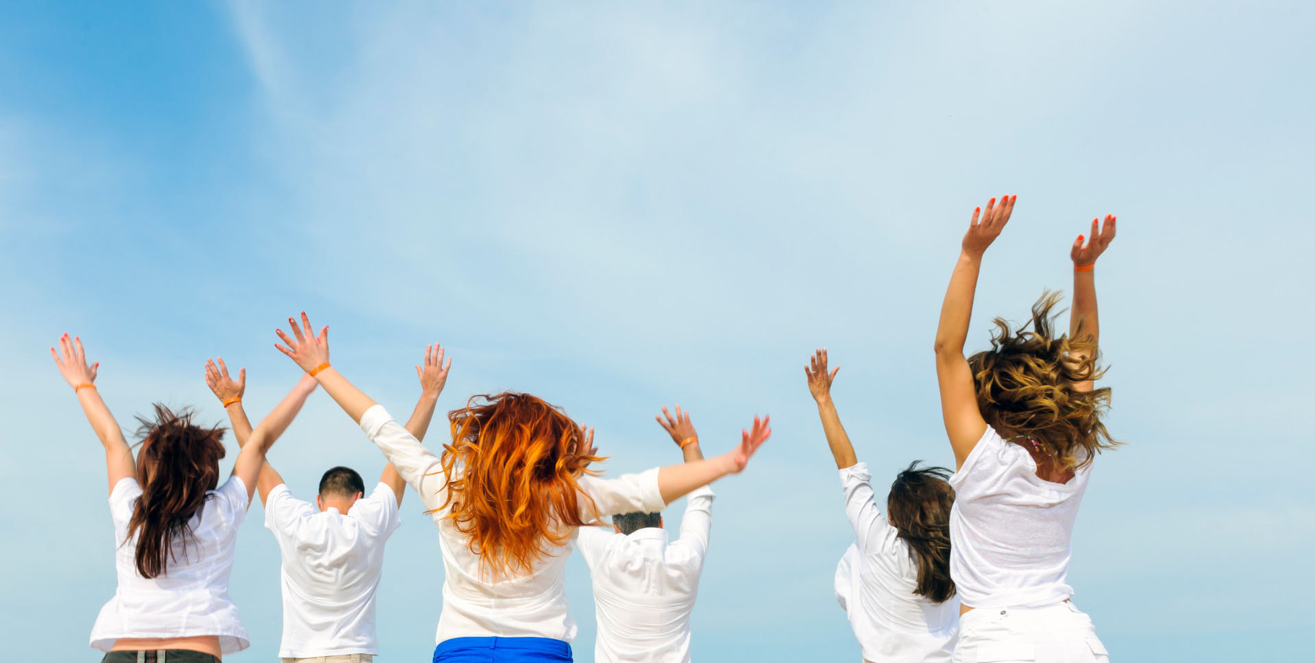 A group of people in white clothes raising their arms in joy on a sunny day, with a clear sky in the background.