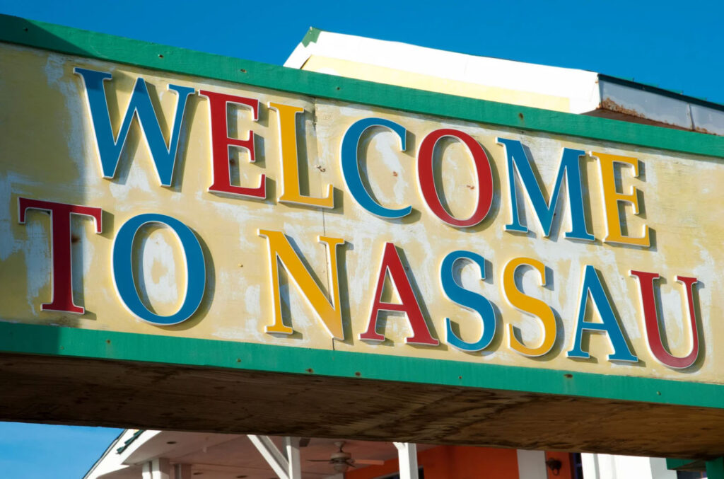 A colorful "Welcome to Nassau" sign, featuring bold letters in red, yellow, and blue, set against a clear blue sky, welcoming visitors to Nassau, Bahamas.
