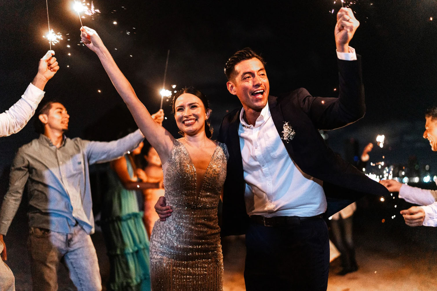 Newly married couple celebrating at a wedding exit, smiling and holding sparklers surrounded by guests, symbolizing joy, celebration, and newlywed energy.