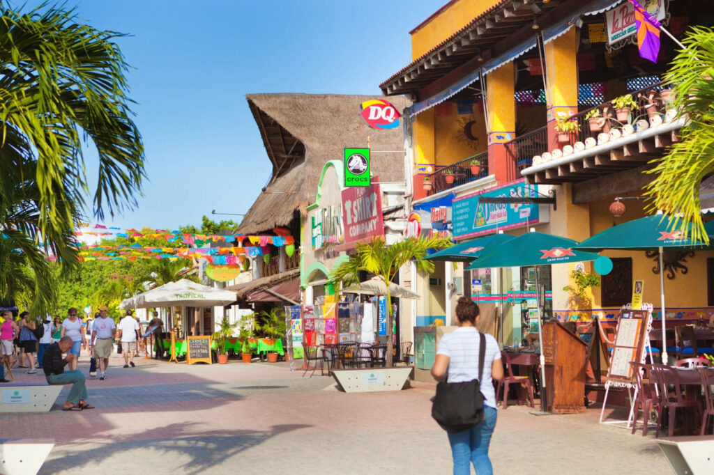 Pedestrian street in Playa del Carmen’s Quinta Avenida, lined with colorful shops, restaurants, palm trees, and people walking through the lively Riviera Maya shopping and dining district.