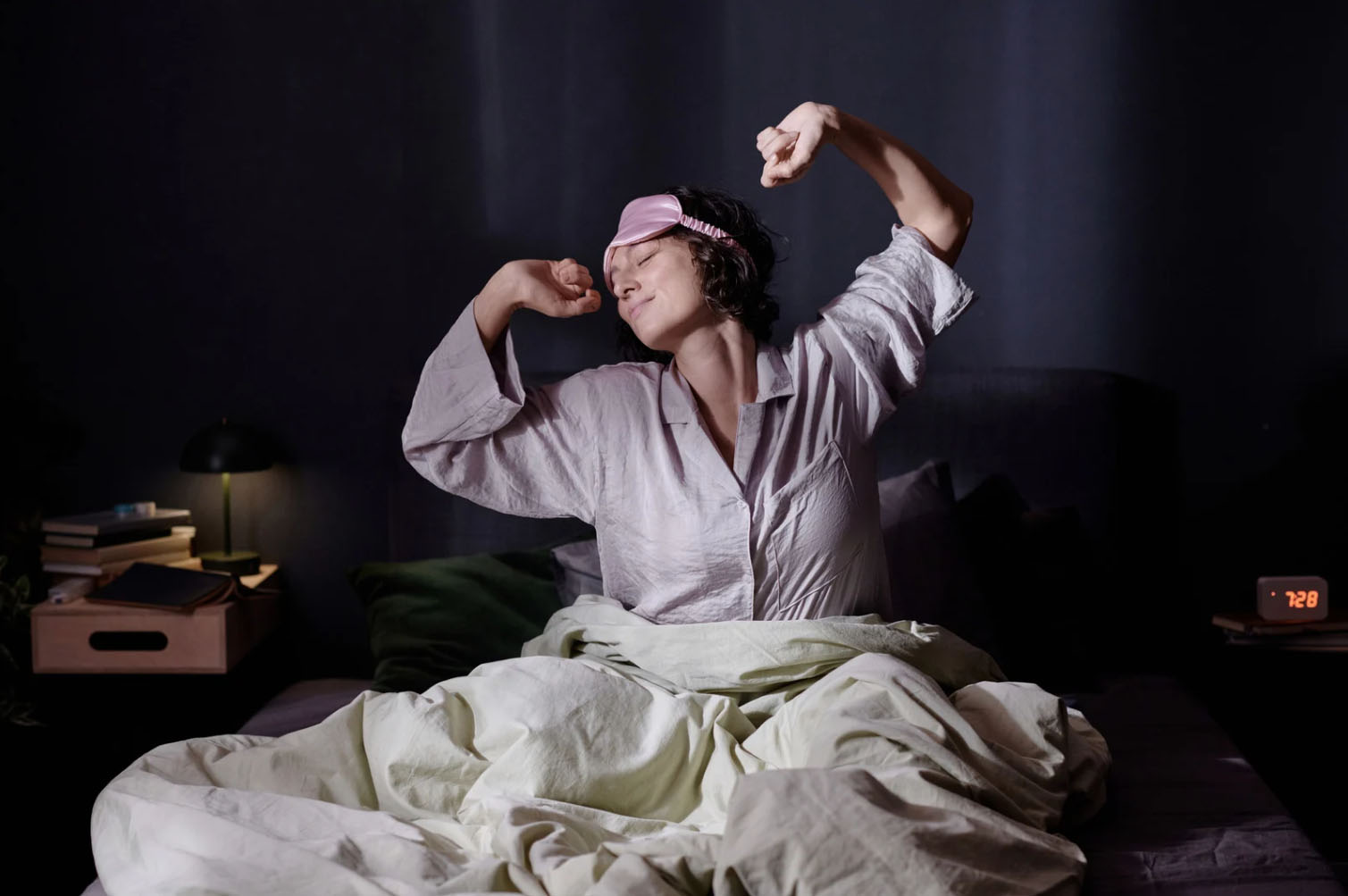 Person stretching and waking up in bed wearing sleepwear and an eye mask, symbolizing restful sleep, recovery, and morning wellness.