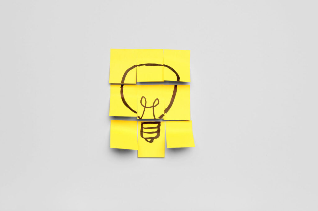 A creative arrangement of yellow sticky notes on a gray background, forming a lightbulb drawing.