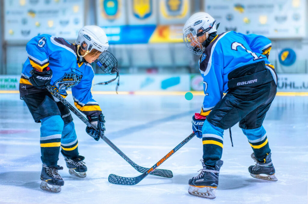 Two young hockey players in blue uniforms compete for the puck on the ice rink during a match.