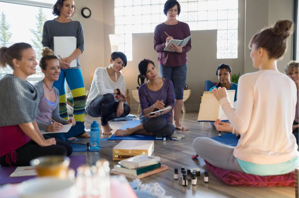 Wellness instructor leading a small group session indoors, with participants seated on mats taking notes, symbolizing group education, mindfulness, and holistic health.