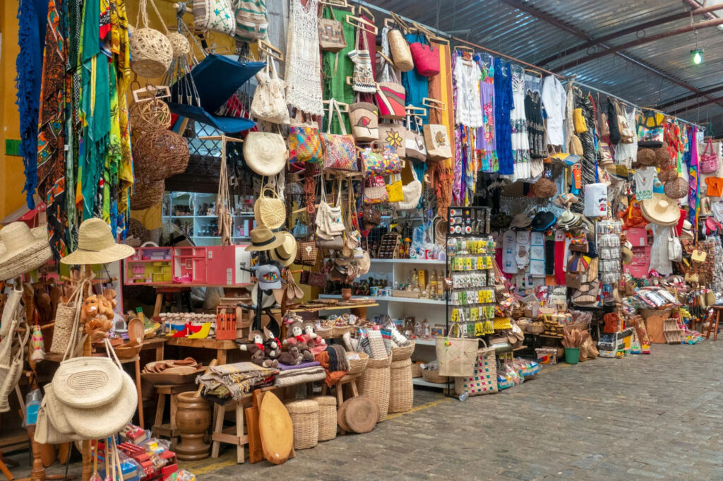 Colorful market stall filled with handmade crafts, woven straw bags, hats, textiles, and souvenirs displayed at a traditional Caribbean artisan market.