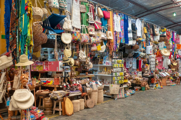 Colorful market stall filled with handmade crafts, woven straw bags, hats, textiles, and souvenirs displayed at a traditional Caribbean artisan market.