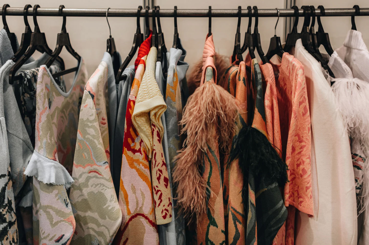 A collection of colorful fashion pieces, including textured and feathered garments, hanging on hangers in a clothing store or boutique.