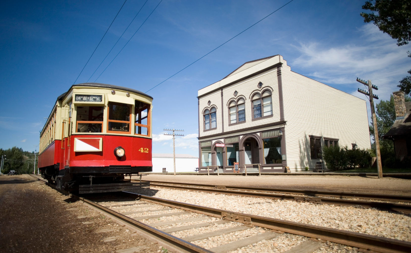 A historic streetcar marked with "42" sitting on tracks next to a vintage building in a historical setting, with clear skies and power lines overhead.