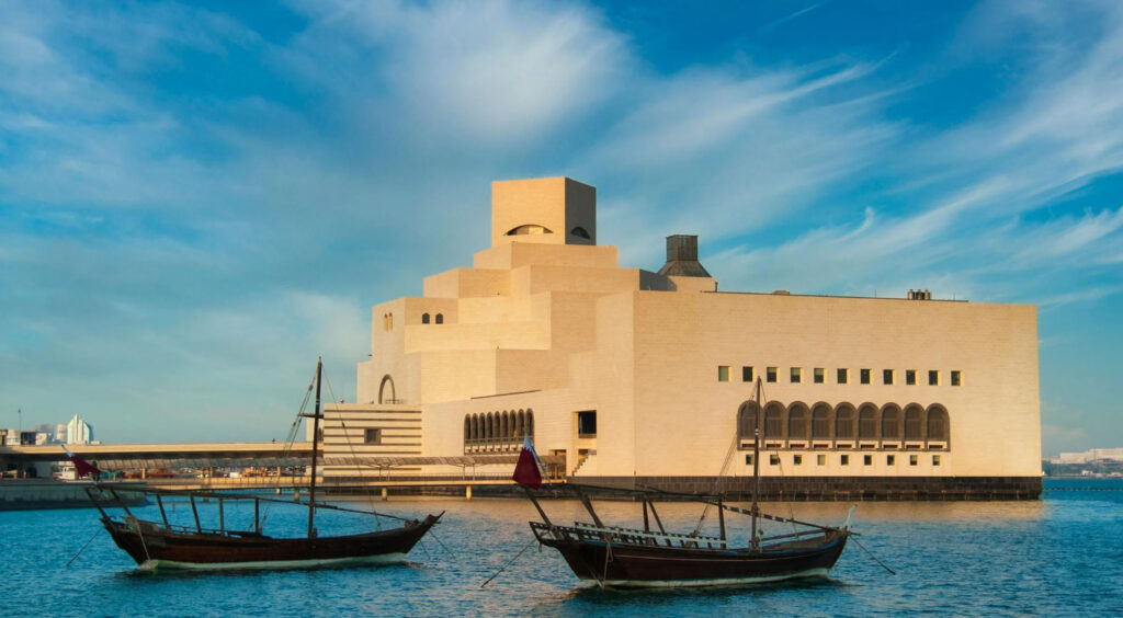 Museum of Islamic Art in Doha, Qatar, featuring I. M. Pei’s geometric limestone architecture beside the waterfront, with traditional wooden dhow boats in the foreground.