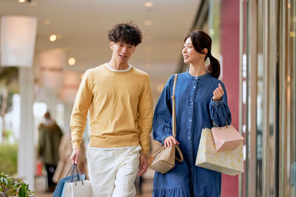 A young couple shopping together at a mall, carrying shopping bags and smiling as they walk.